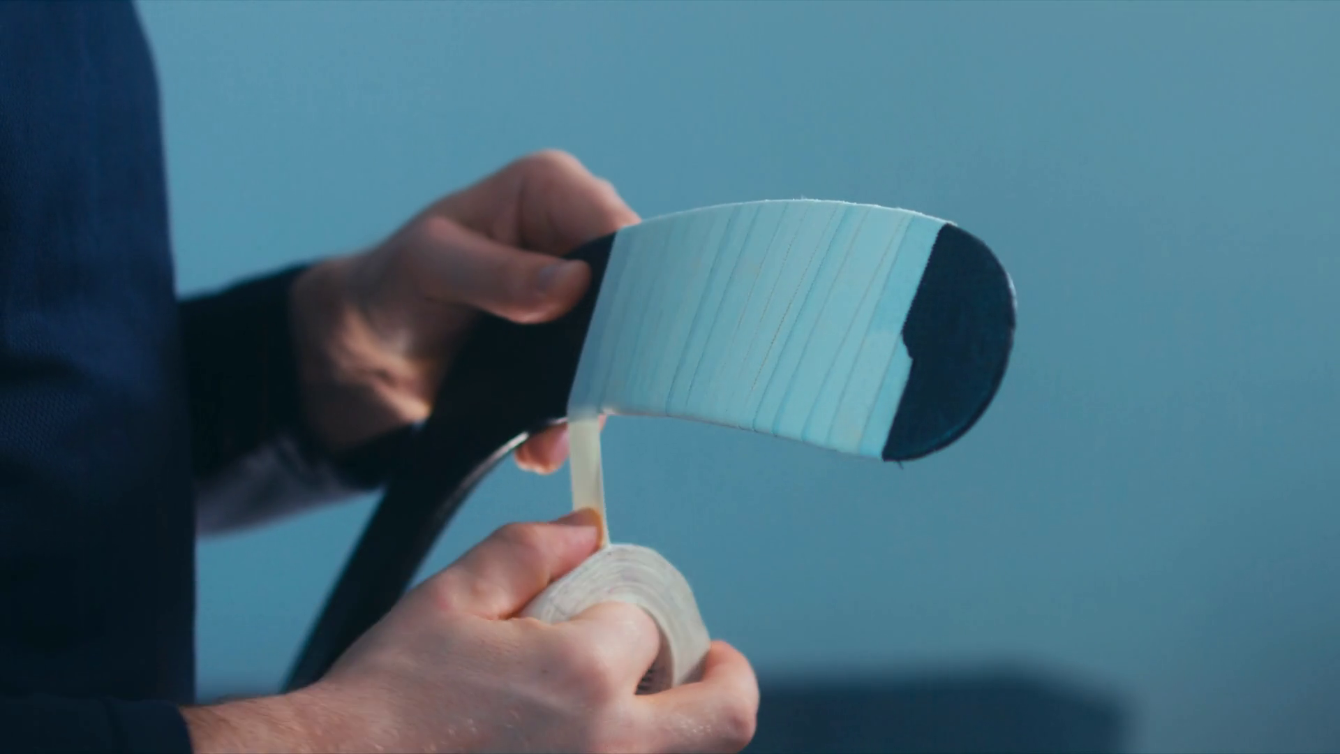 CU Caucasian male ice hockey player taping a stick blade, preparing for