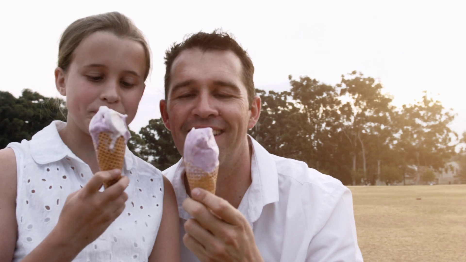 Father and Daughter eating ice cream at sunset in park, steadicam shot