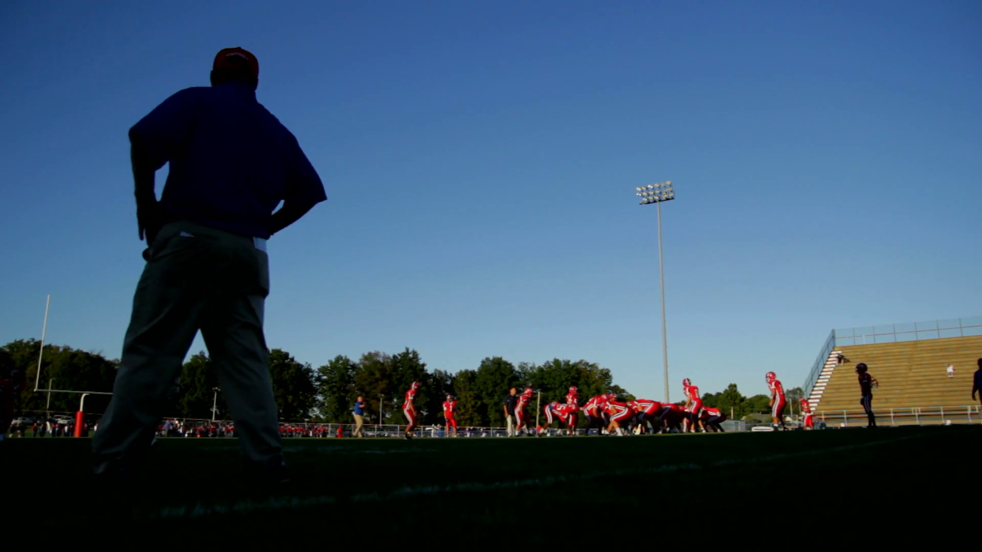 Football players practice a play as their coach watches them from the