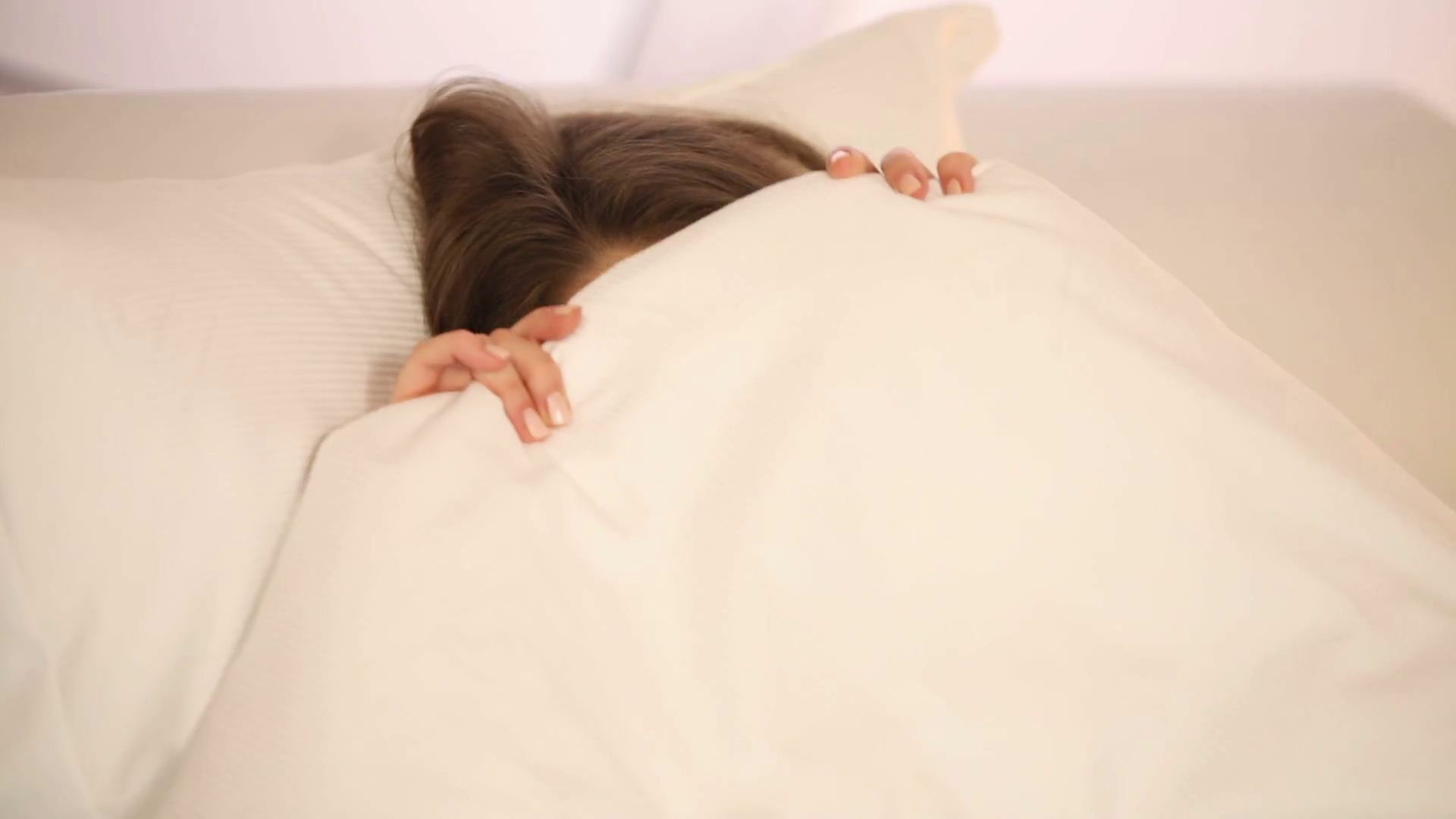 Funny girl lying in bed pulling blanket over her head laughing and