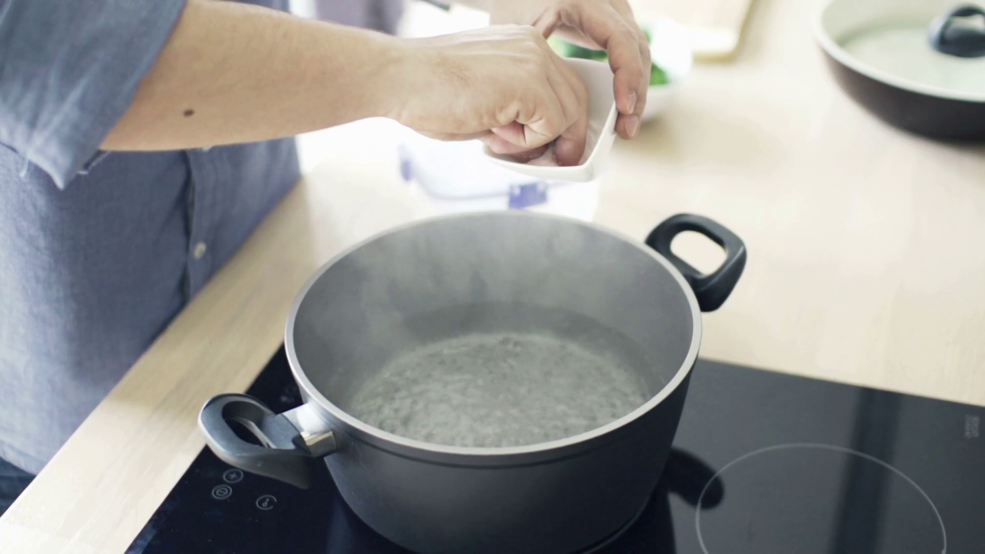 Man boiling water in pot and adding salt in kitchen, slow motion shot