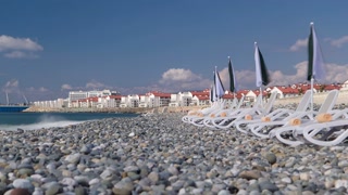 Marine pebble beach with chaise-longue in city Adler timelapse hyperlapse with houses and blue cloudy sky in the background 4K