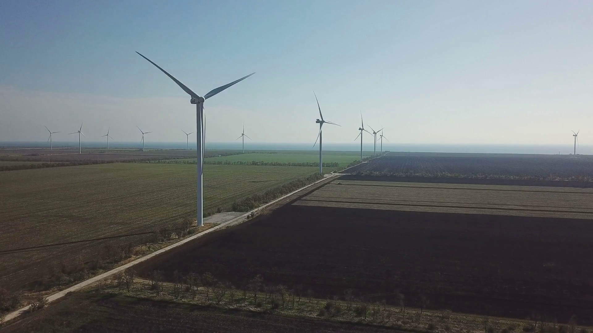 Aerial shot of rotating wind turbines on farmland near ocean Stock