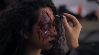 Make-up artist make the girl halloween make upin studio. Halloween face art. Woman applies on professional greasepaint on the face of spanish girl. War-paint with blood, scars and wounds. Slow motion