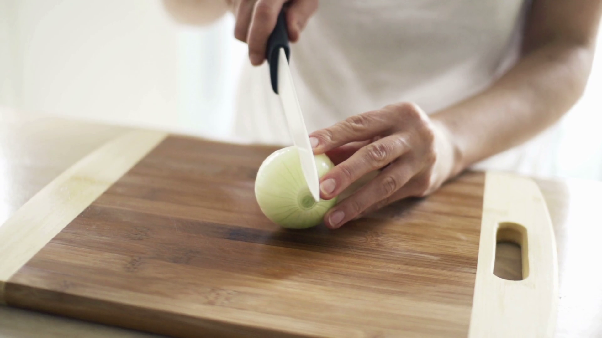 Woman slicing onion on chopping board in kitchen, slow motion shot at