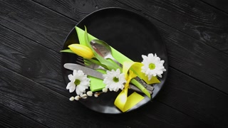 Easter spring table dishware composition with yellow tulip flower. Placed on black handmade ceramic plate. On wooden background.