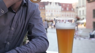 Man drinks Beer sitting at the Table of Street Restaurant in old European City