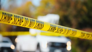 A bright yellow Crime Scene Do Not Cross tape stretched across an urban environment. The car accident. White trucks are driving in the