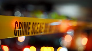 A bright yellow Crime Scene tape across an urban environment, marking a restricted area for investigation. Police flashing lights are on the