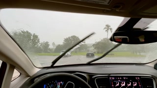Windscreen wipers on a car removing raindrops from the windshield. Wide shot