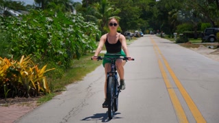 A woman rides a bicycle among green palm trees in tropical suburbs
