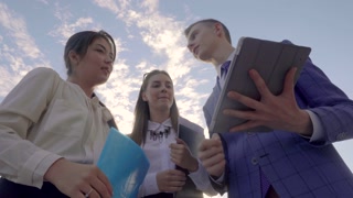 Three Young Professionals Networking and Making Deals, Standing Near Business Center with Skyline Background Outdoors in Neutral Tones.
