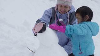 Mother and daughter building snowman together