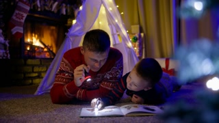 Cinematic RED camera shot father and boy playing with flashlights in living room in canvas tent with Christmas tree and stockings decoration