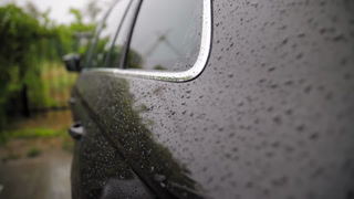 Raindrops trickling down the side surface of a modern black car during heavy rain. Close-up abstract texture.