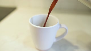 Coffee being poured from metal French press into white cup on kitchen counter