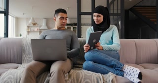 Muslim woman and husband work on devices in living room
