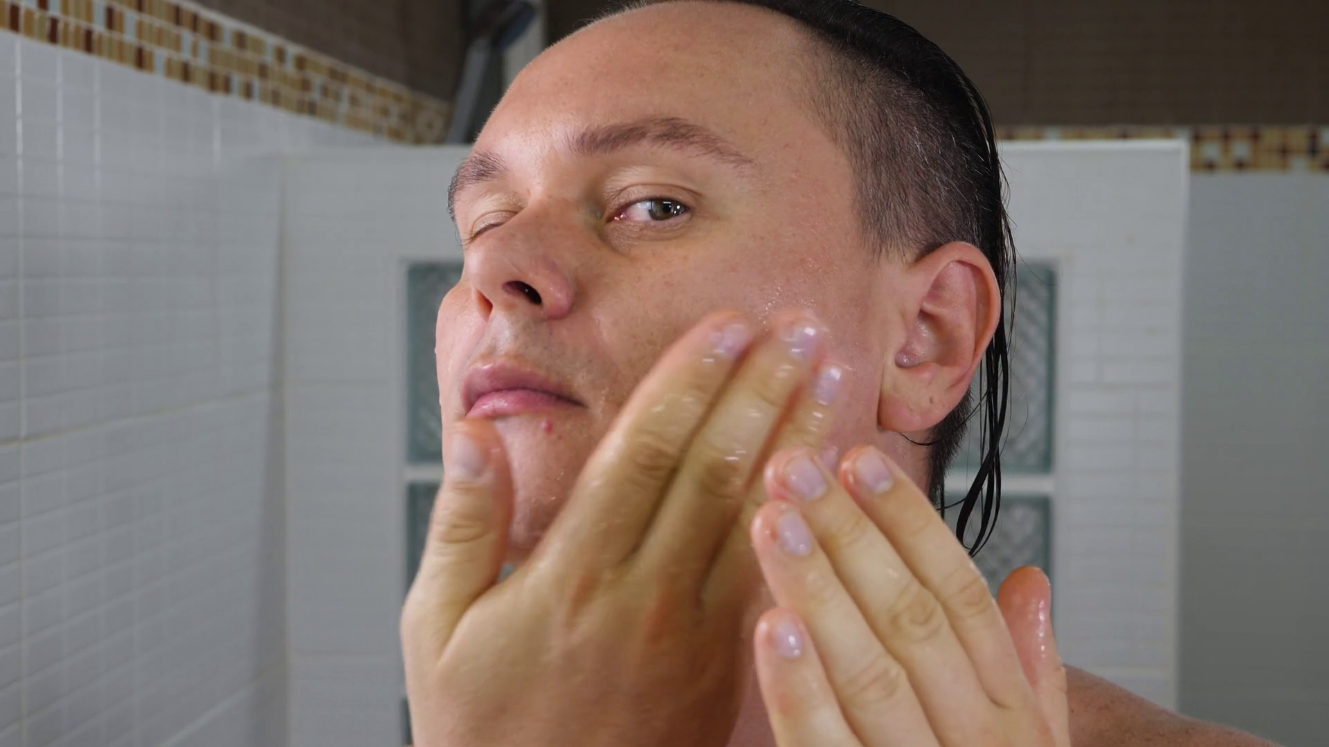 Man apply cream after shaving face in bathroom looks in mirror. Morning routine. Man grooming