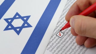 Hand voting in paper ballot by red pencil in Israel wirh Israeli flag
