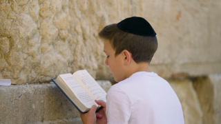 Jewish boy with a yarmulke praying and reading a holy book at the Wailing Wall in Jerusalem
