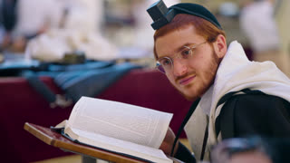 Young Hasidic Jewish man with tefillin and tallit praying in a synagogue