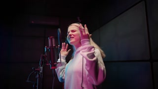 Beautiful lady singing loudly in recording studio, portrait of female singer. Lady with headphones and microphone. Talented and inspired