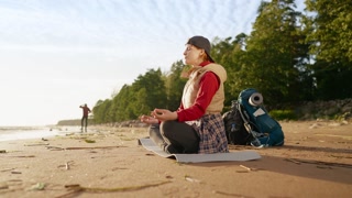 Recovery of vitality and balance, young woman traveler resting after hiking. Female tourist sitting on sandy of lake and practicing