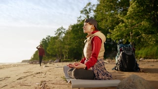 Portrait of relaxed woman traveler on seacoast, breathing exercise for relax. Young adult woman sitting in lotus position outdoors and