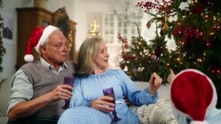 Fabulous winter holidays, family celebrating Christmas. Happy little boy in Santa hat talking with grandparents in foreground.