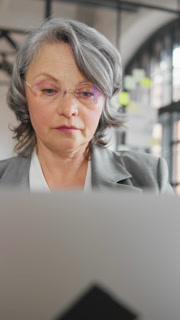 Charming grey-haired lady working in office, closeup vertical portrait, work and life balance. Career in modern company, successful business