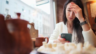 Woman in cafe window using phone to communicate and read
