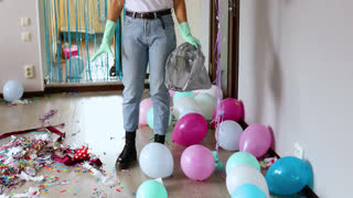 Woman cleaning mess of floor in room after party, removes garbage from the floor, disposable cups in a bag, morning after party celebration, housework, cleaning service