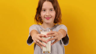 Pretty teen girl, child with a fresh glass of milk isolated on studio yellow background, strong bones, milk for growth, healthy lifestyle concept, copy space