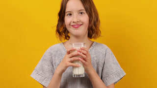 Pretty teen girl, child with a fresh glass of milk isolated on studio yellow background, strong bones, milk for growth, healthy lifestyle concept, copy space