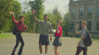 Group of cheerful diverse multiracial college students waving goodbye to classmates, expressing friendliness and positivity while walking after finishing lesson at campus.