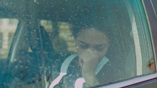 Emotionally stressed pensive african woman in deep thoughts sitting in driver's seat and looking through car window with raindrops, staring with depressed expression, full of melancholy and sadness.