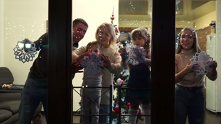 Parents and children gluing paper snowflakes to windows, Christmas tree standing in center of room, footage from outside. Happy family decorating home for festive season together. Concept of holiday