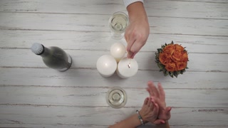 The couple of lovers lights candles on the wood table whith flowers, drinks wine, takes hands and spends a romantic evening together. Top view. Hands close up view. St. Valentine's Day