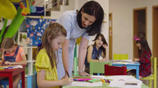 Creative kids during an art class in a daycare center or elementary school classroom drawing with female teacher.