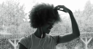 Woman listening to music and shaking her hair in front of background with raindrops on the glass