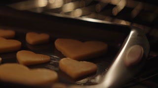 Young woman bakes and decorates heart shaped cookies with icing and sprinkles for valentines day