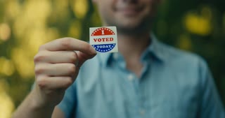 Young man smiling with an I Voted sticker and pin 