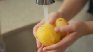 Woman washing lemons in the kitchen sink. Slow motion, close up.