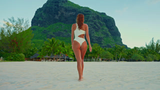 A concept of luxury vacation, freedom, beauty and tropical travel lifestyle. Ideal for summer promo content. View of woman walking along a