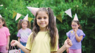 Birthday girl in colorful t-shirt holding her birthday gift and smiling, outdoors birthday party with happy kids and holiday decorations in summer garden