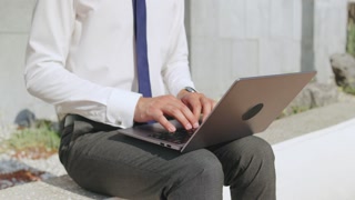 Business professional working on laptop outdoors in a modern urban setting during a sunny day