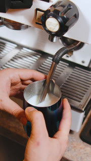 Barista steaming milk for coffee at an artisan cafe during morning rush