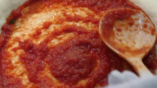 Chef spreading fresh tomato sauce on raw pizza dough with a ladle, close-up of authentic Italian pizza preparation.