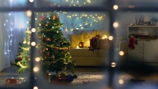 Beautiful Moving Shot From a Snowy Street Into the Window. Seeing Decorated Christmas Tree with Gifts Under It and Lots of Christmas Lights in the Room with cozy Celebratory Atmosphere.