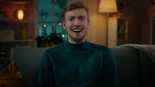 Portrait of a Handsome Man Sitting on a Couch at Home at Night, Watching Comedy Series on TV. Man Has Really Good Fun Watching Movie.